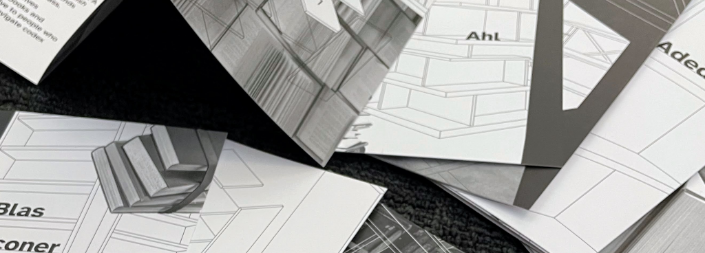 Black and white print issue cards laid out on a flat surface showing different folds and the shadows each of the cards have on one another. Photo shows the thickness of the paper used for the print issue.