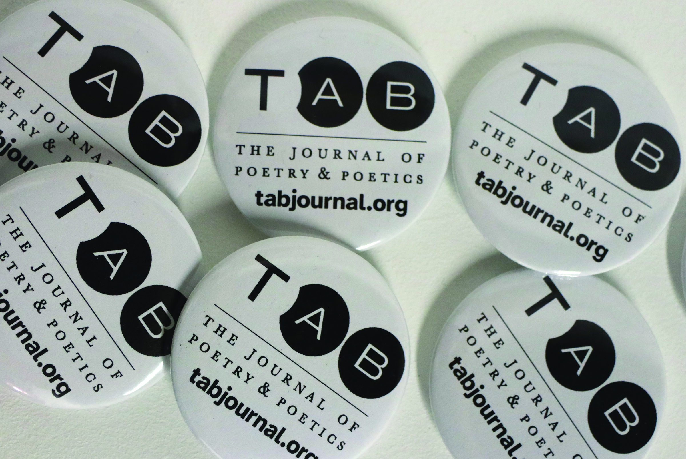 A collection of circular pinback buttons featuring the TAB Journal logo — a bold 'TAB' design with a black circle — along with the text 'The Journal of Poetry & Poetics' and 'tabjournal.org' on a white background