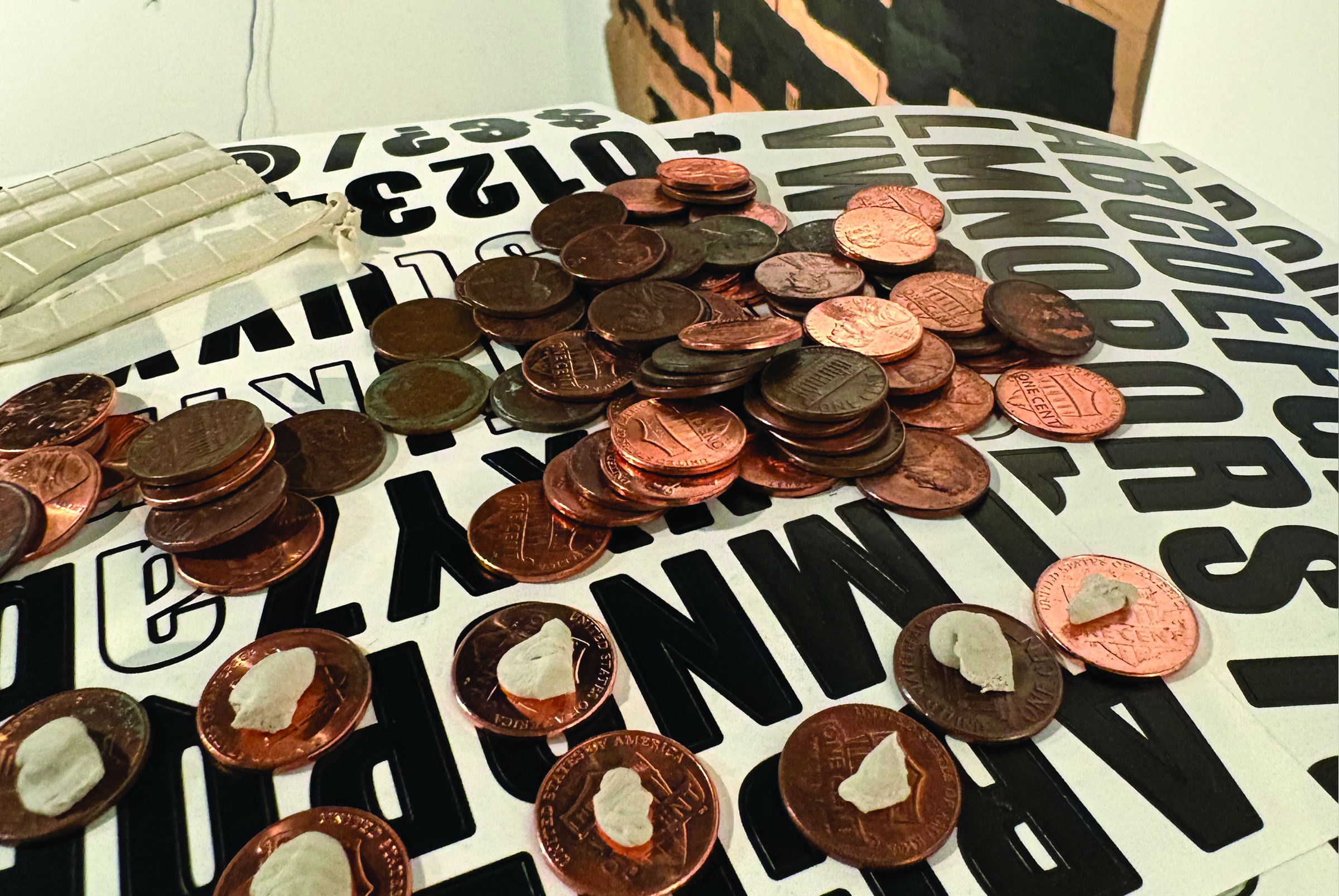 A large pile of copper pennies scattered across a flat surface printed with oversized black block letters and numbers, suggesting a typographic or letterpress background.