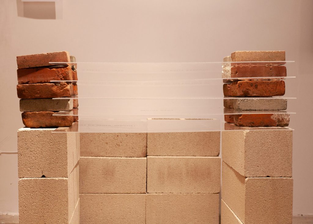Side view of stacked cinder blocks and bricks holding up 5 thin layers of plexiglass