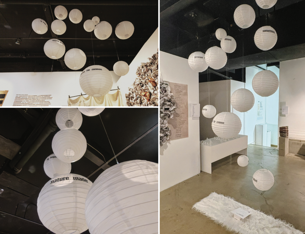 Multiple white spherical paper lanterns suspended from the ceiling at varying heights, illuminated from within, hanging above a white rectangular platform on the floor.