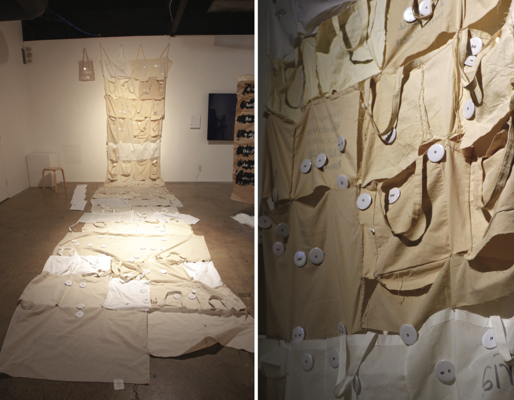 Tote bags that have been roughly attached to one another creating a tapestry from height of ceiling extending far onto the bottom of the floor. Buttons with black lettering are arranged mimicking the poem's composition