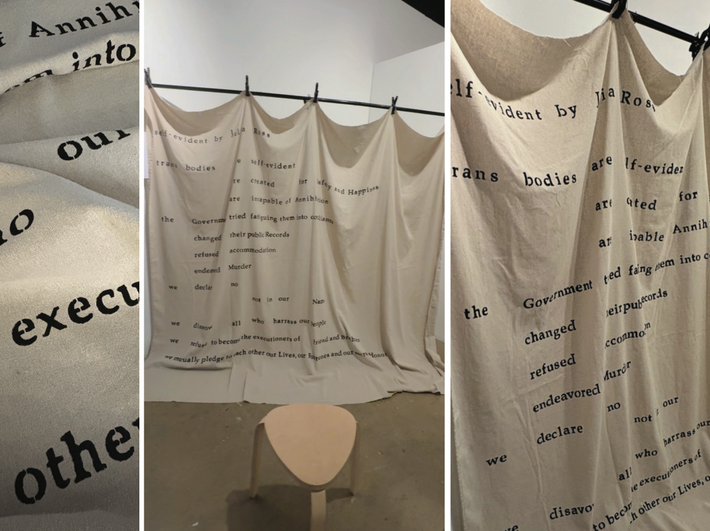 Large canvas hanging from a horizontal rod, with hand stenciled text running across them in thin lines. A small wooden stool sits below.